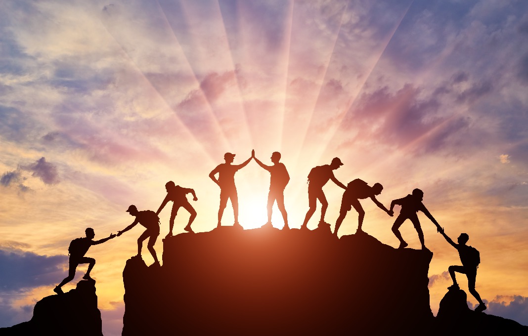 Members of a team helping each other to the top of a mountain