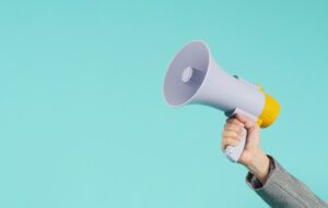 Hand holding megaphone and wear grey suit on green background.