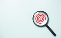 Red dartboard inside of black magnifier glass on blue background