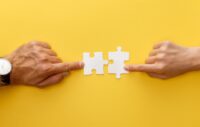 cropped view of woman and man matching pieces of white jigsaw puzzle on yellow background