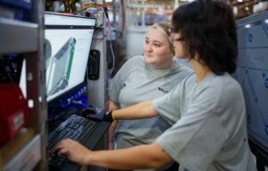 Two employees in front of a computer screen on manufacturing floor