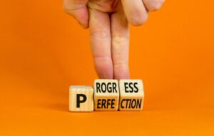 Businessman turns cubes and changes the concept word 'perfection' to 'progress' on an orange background.