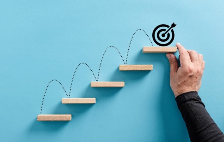 hand arranges a wooden block staircase with target icon.