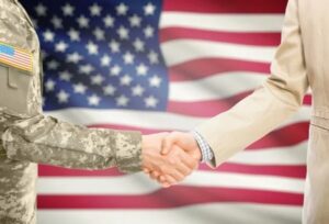 Business person and military personnel shaking hands in front of American flag