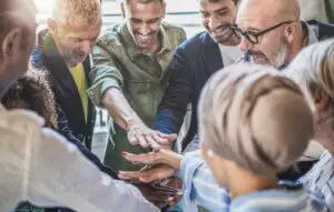 Diverse business team stacks hands in unity, showcasing teamwork and partnership in a dynamic workplace.