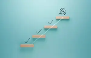 Wooden steps with check marks leading to a ribbon icon on a turquoise background
