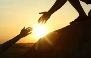 Hiker helping friend outdoors at sunset.