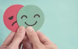 Hands holding sad face hiding behind happy face