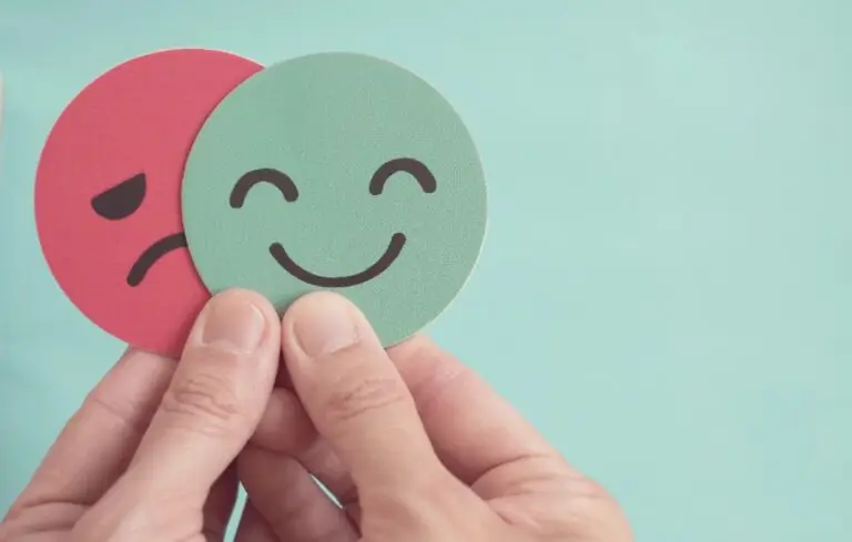 Hands holding sad face hiding behind happy face