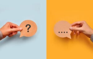 hands holding paper cutout speech bubbles with question mark and ellipses