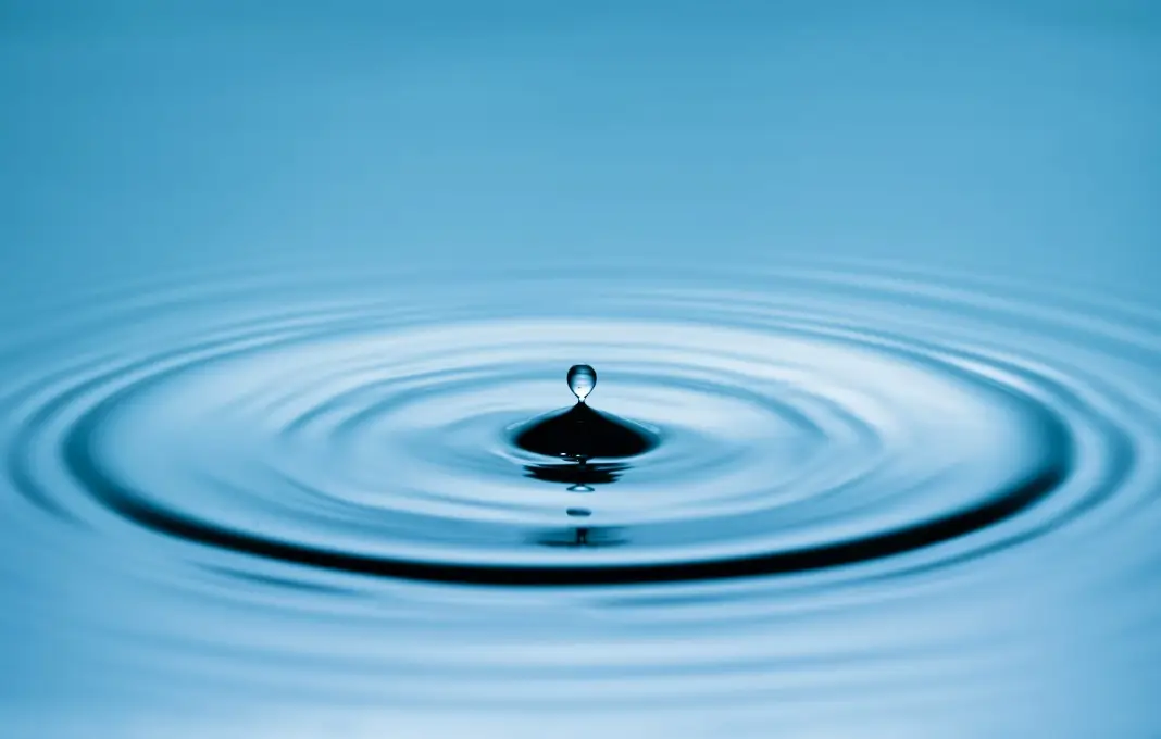 Close up of a blue water drop macro creating concentric ripples on a calm water surface.