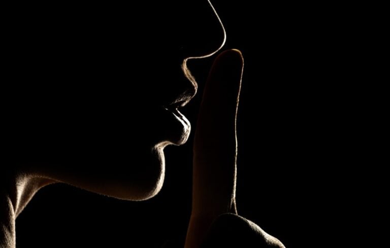 Silhouette of unknown woman , face in the shadow holding finger on her lips on a black background
