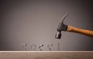 Line of bent nails and a hammer above an unbent one