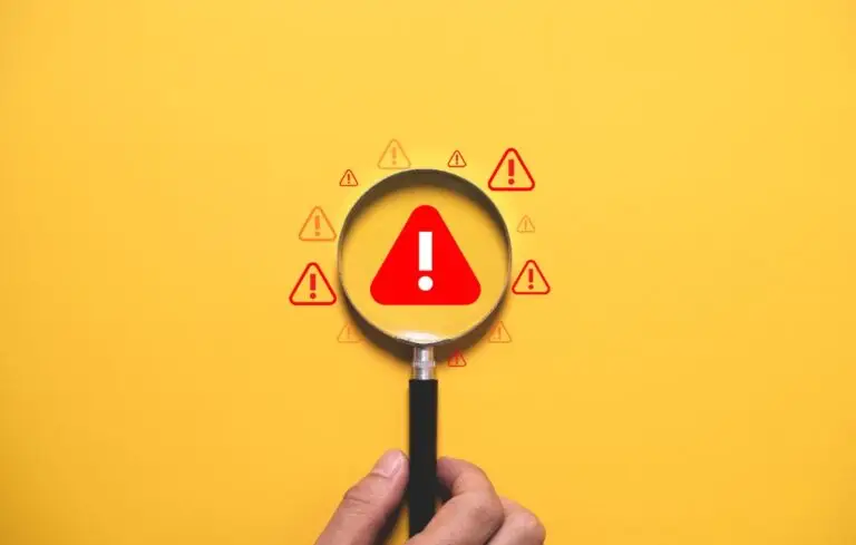 Warning alert concept with magnifying glass focusing on danger symbol over yellow background.