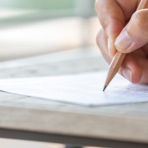 Student hand testing doing test exam with pencil drawing selected choices on answer sheet in school final exams at college or university. Taking multiple choice for assessment in examination classroom