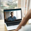 Rear view close up businesswoman chatting with colleague online in office, using laptop, confident businessman brainstorming project, hr manager holding interview with candidate by video call